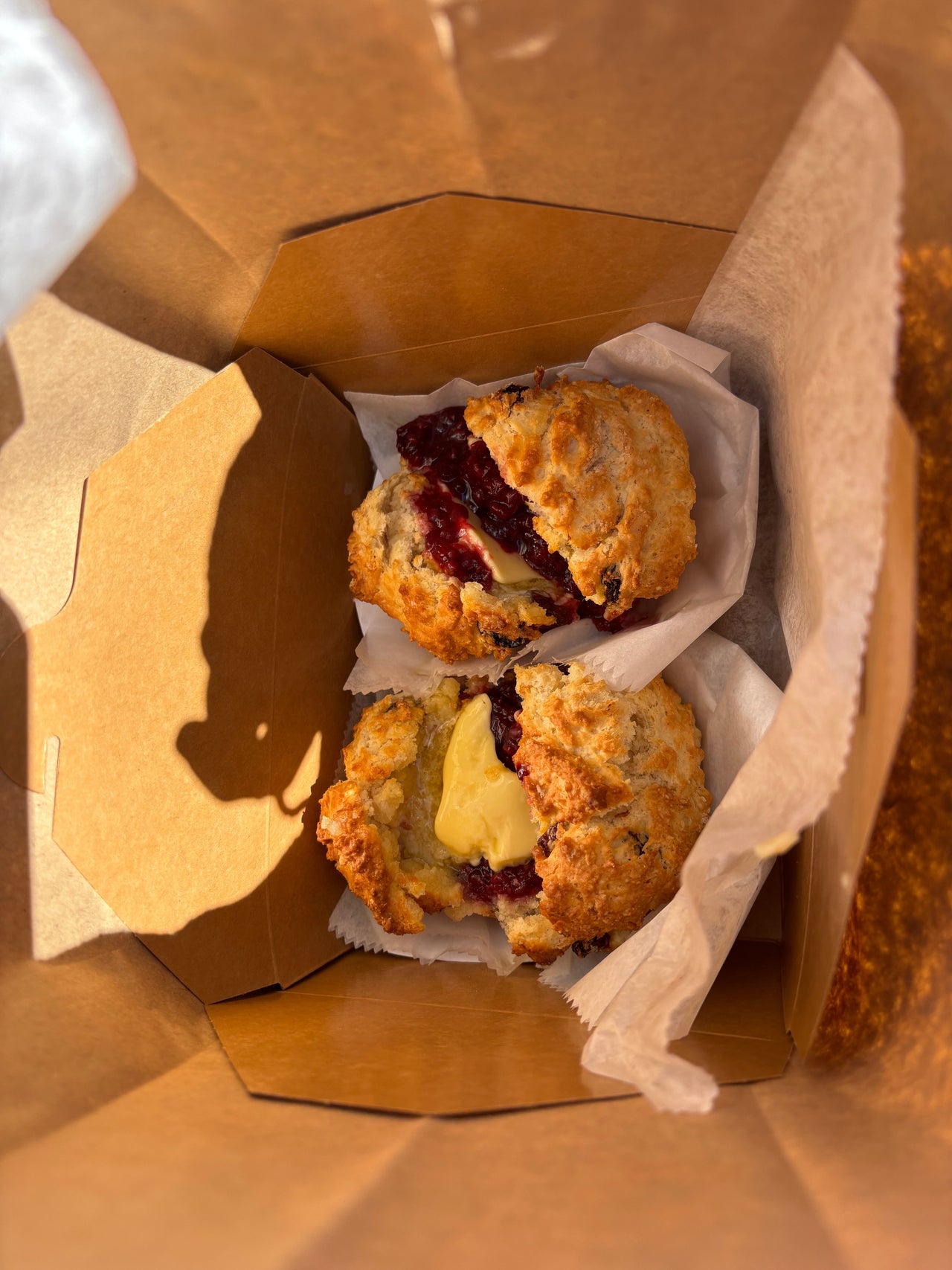Two warm, freshly baked Irish scones split open with melting butter and blackberry jam, awaiting love on a New York East Village street, with the small bakery storefront and line of customers no longer in view.
